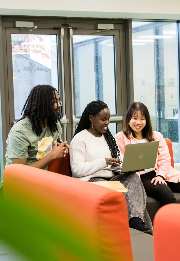 Three international students, one male and two female, look at a laptop together