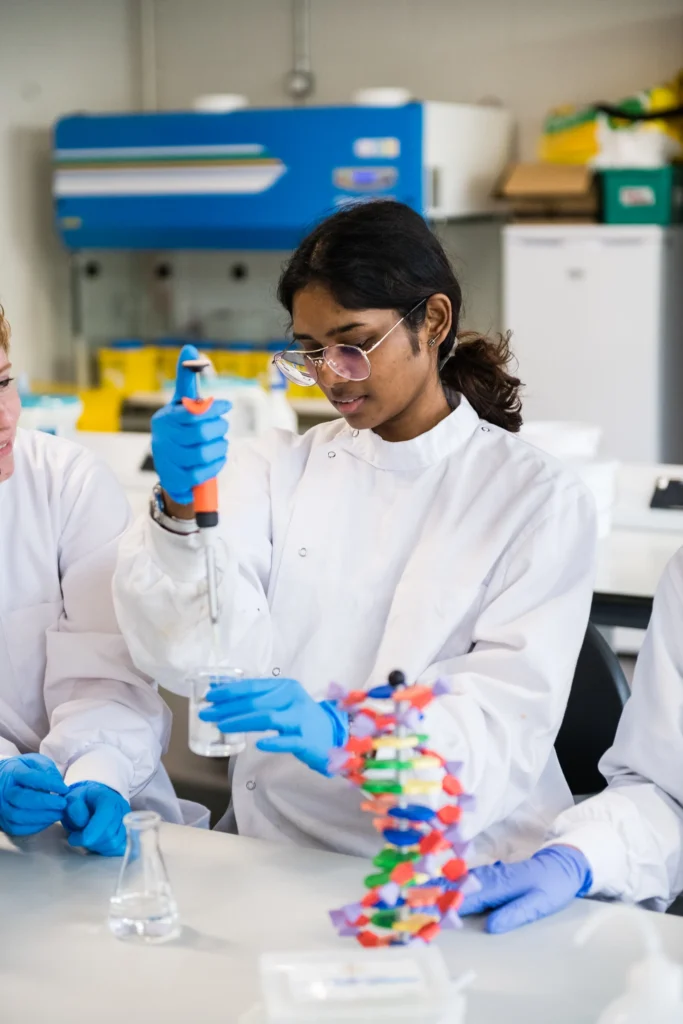 Female international student in lab coat uses a pipette in the laboratory surrounded by lab equipment