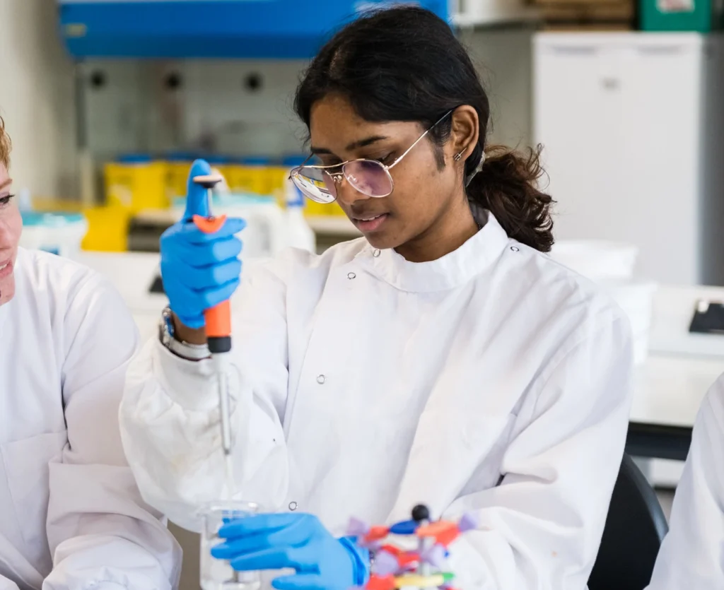 Female international student in lab coat, using a pipette and laboratory equipment