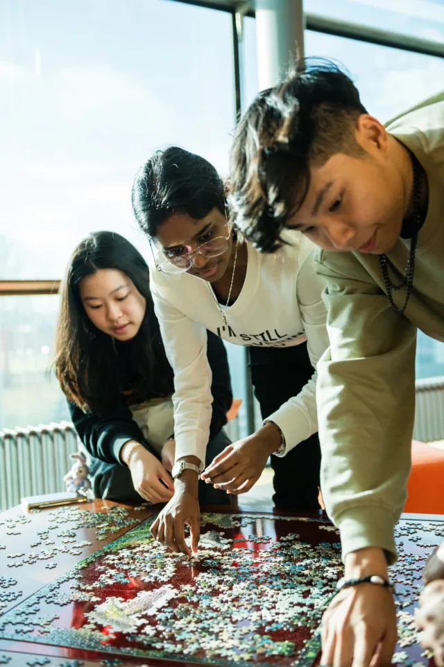 Three students standing over a coffee table making a jig-saw together