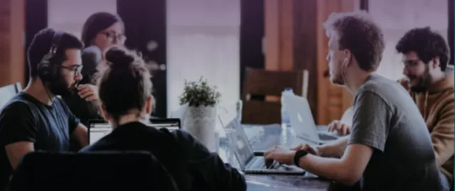 Image of students sitting around a desk working on laptops