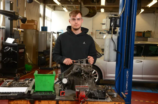 Male student at work bench wearing goggles in learning garage.