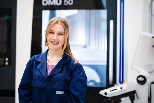 Female student in navy overalls stands in engineering workshop