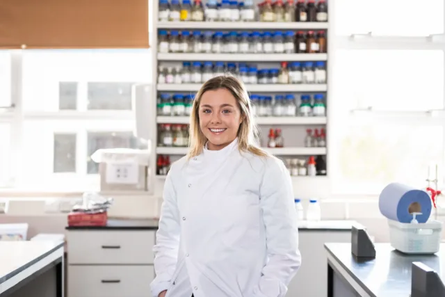 Student in white lab coat stands in lab in St Angelas