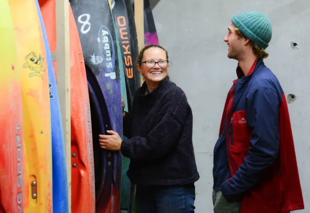 Female and male outdoor education students stand beside colourful surfboards