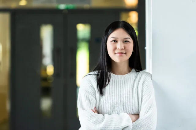 Female student stands arms crossed in campus corridor