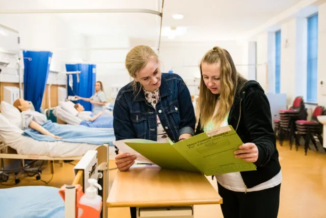 Two nursing students reviewing medical charts in hospital classroom